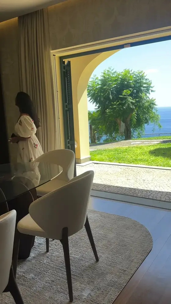 Sala de jantar de uma moradia com arco aberto para o jardim e o mar, cadeiras claras e mesa de vidro
