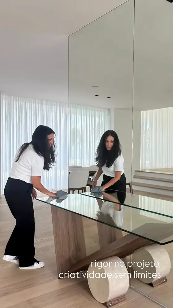 Duas pessoas medem uma mesa de vidro numa sala com espelhos